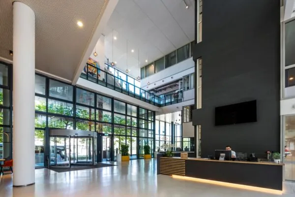 Moderne en ruime entreehal van een kantoorgebouw aan de Thomas R. Malthusstraat met glazen gevel, ontvangstbalie en vide.